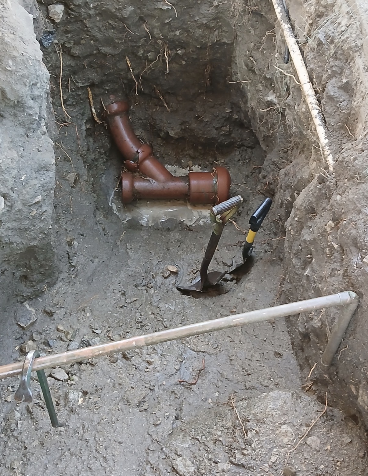 Old corroded cast iron drain pipe exposed in trench